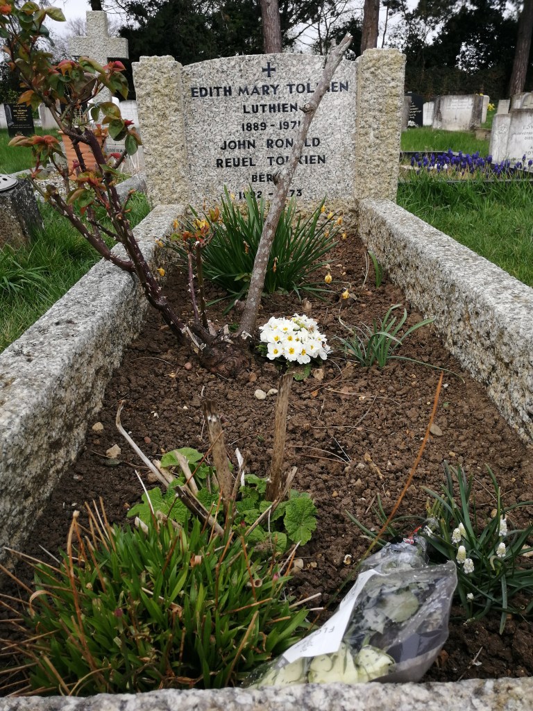 Image shows JRR and Edit Tolkien's grave. It is white with flecks of black. 
Plants and flowers sit on the earth in front of it.