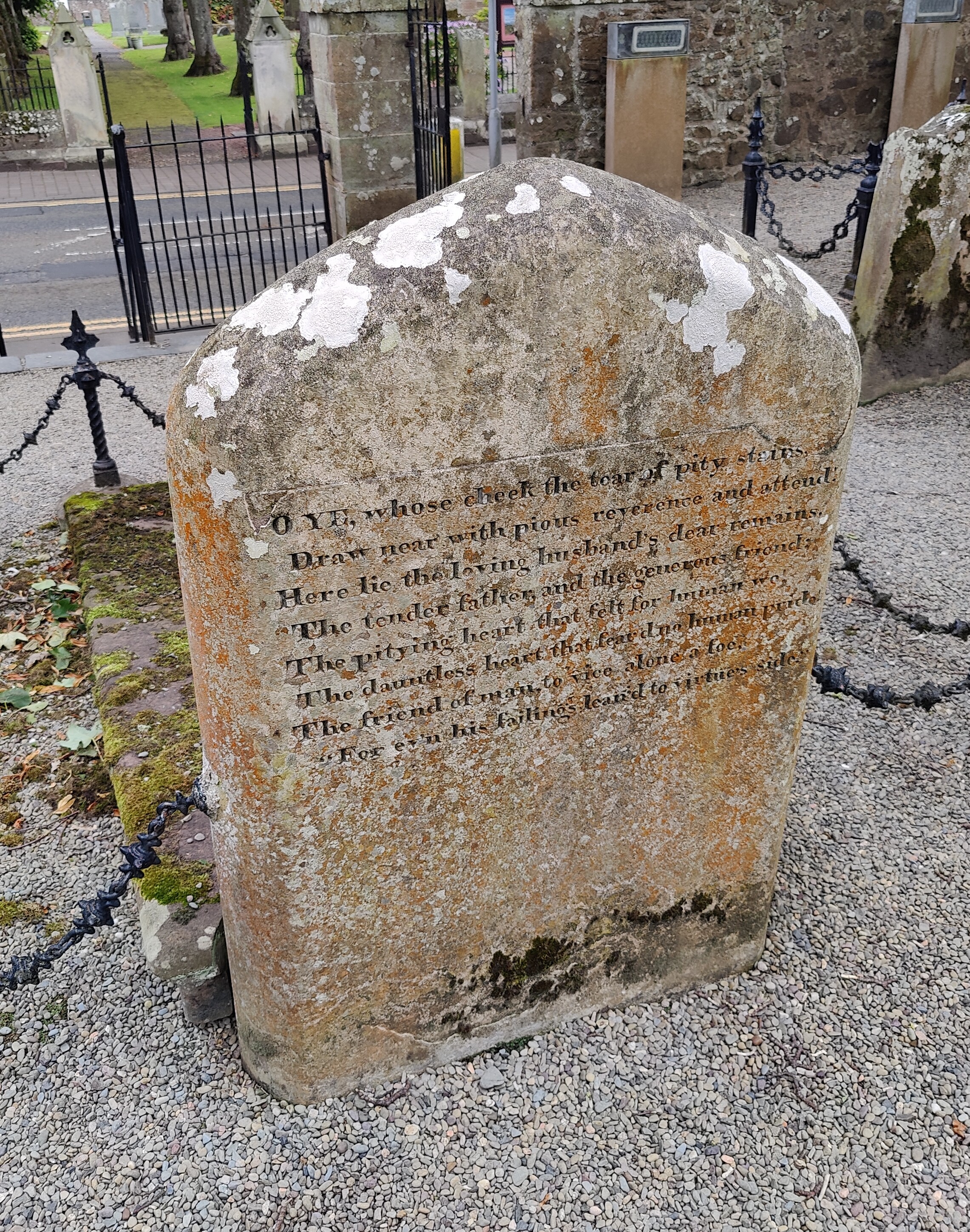 On the back of a stone gravestone is an inscription that reads "O YE, whose cheek the tear of pity stains,
Draw near with pious reverence and attend! Here lie the loving husband's dear remains,
The tender father, and the generous friend;
The pitying heart that felt for human wo!
The dauntless heart that fear'd no human pride!
The friend of man, to vice alone a foe,
For ev'n his failings lean'd to virtue's side."