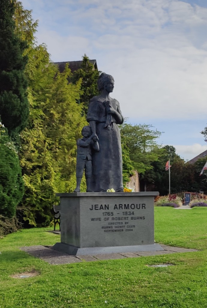 
Grey stone statue of Jean Armour. Woman holding hand of small child. Inscription reads "Jean Armour. 1765 - 1834. Wife of Robert Burns. Burns HOWFF Club. September 2004"